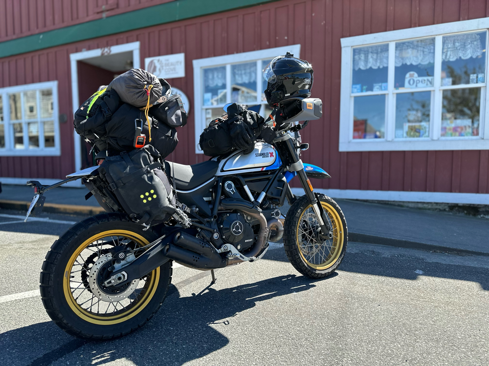 Lucia the Ducati Scrambler packed with luggage outside a store.